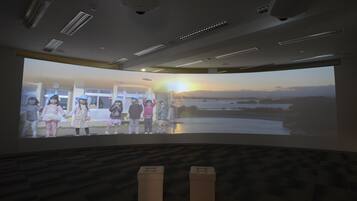 Un écran de projection diffusant une scène de coucher de soleil où des personnes se tiennent la main.