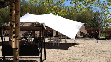 Een rustieke buitenruimte met een grote witte luifel, houten tafels en stoelen.