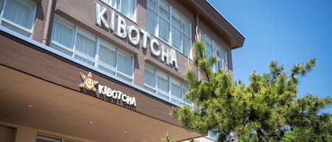 A hotel named "KIBOTCHA" with a modern facade, large windows, and a sign with a sun icon.