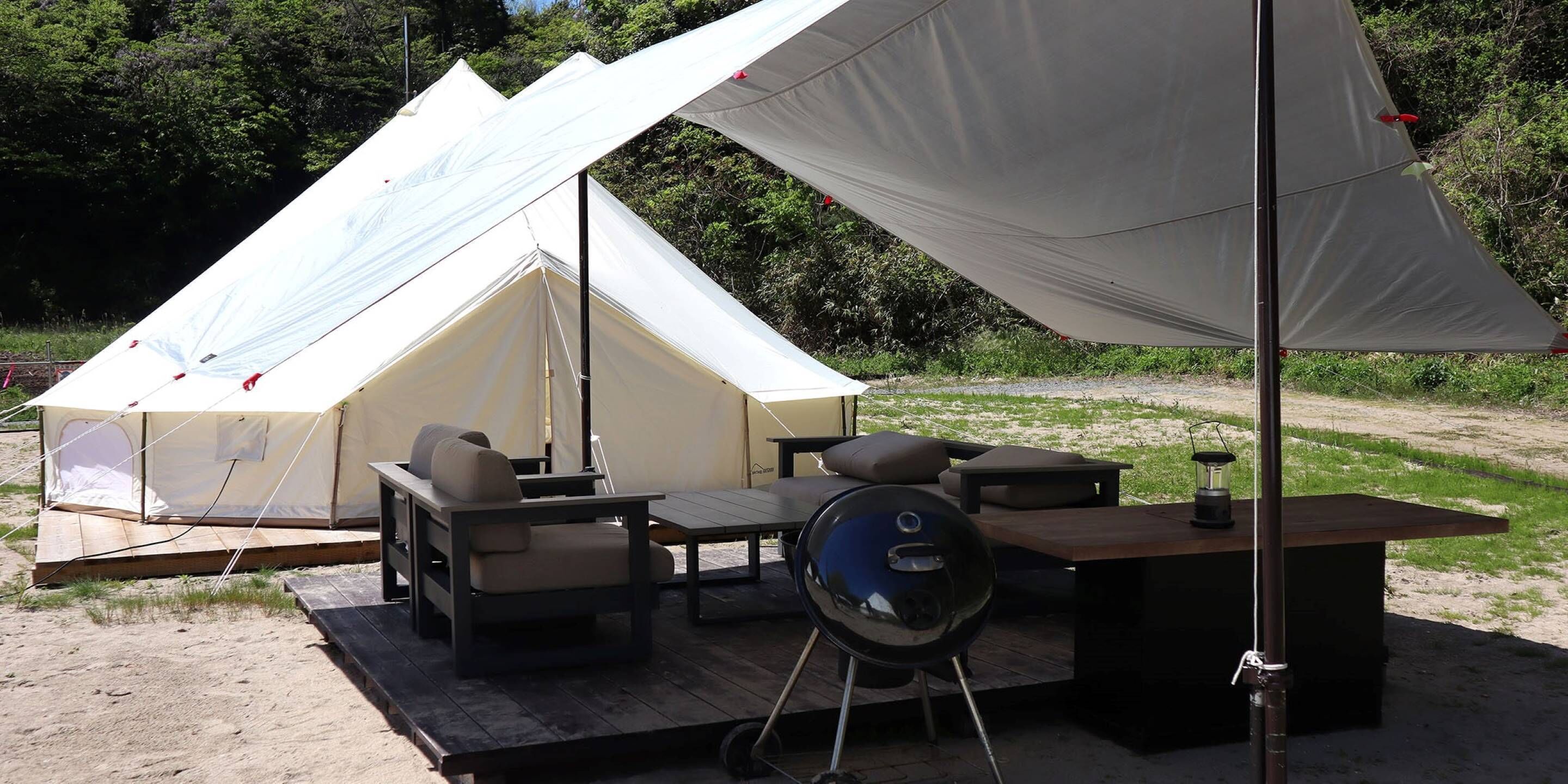 Uma tenda com mesa, cadeiras, churrasqueira e um candeeiro.
