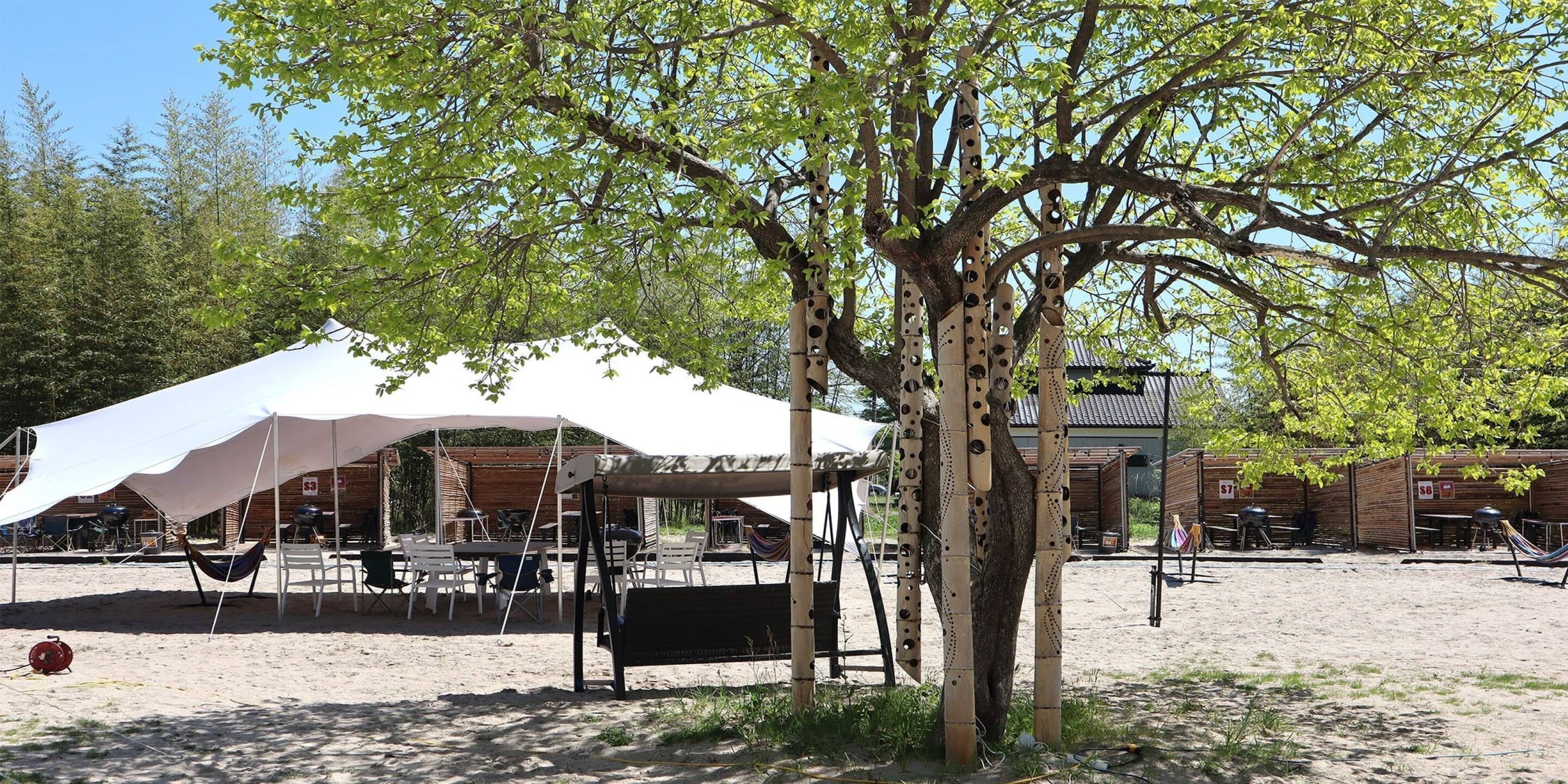 A campsite with a white tent, tables, chairs, and a hammock.