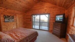 A wooden cabin bedroom with a bed, a dresser, a television, and a sliding glass door leading to a balcony. - Mountain Top Private Retreat (todd)