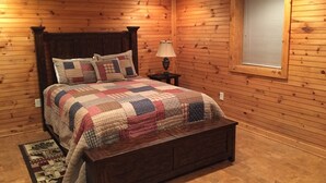 A wooden-paneled bedroom with a large bed, a nightstand, a lamp, and a window with blinds. - Mountain Top Private Retreat (todd)