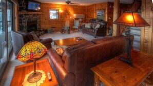 A cozy log cabin interior with a stone fireplace, leather sofas, a wooden coffee table, and a stained glass lamp. - Mountain Top Private Retreat (todd)