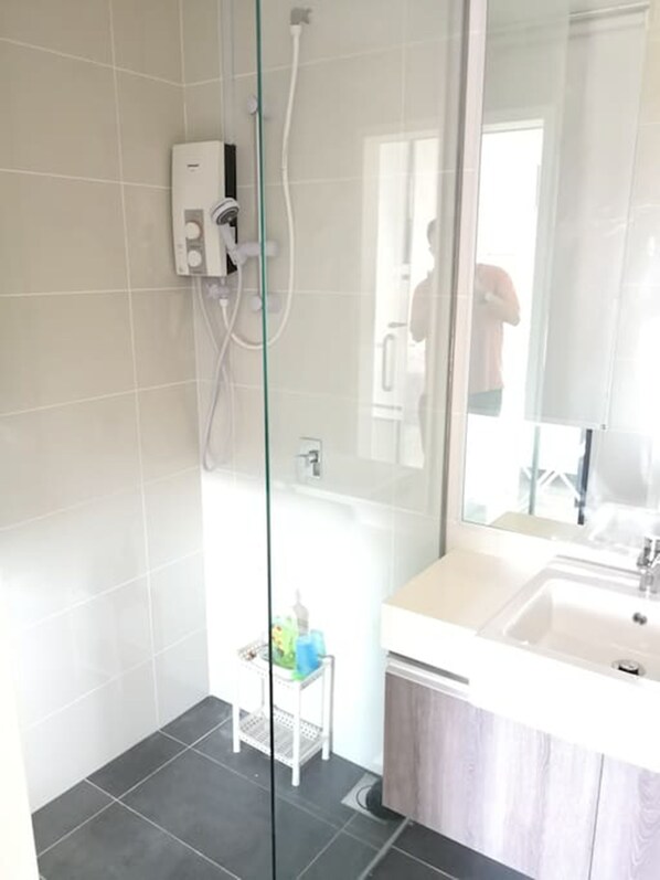 A modern bathroom with a glass shower enclosure, a white sink, and a small step stool. - South Key Mosaic 19 (Johor Bahru)