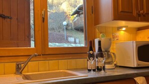 Une cuisine avec des meubles en bois, un évier, un four à micro-ondes et une fenêtre donnant sur une maison et des arbres.