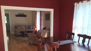 Un comedor con mesa y sillas de madera, un conjunto de sofás y una alfombra estampada.