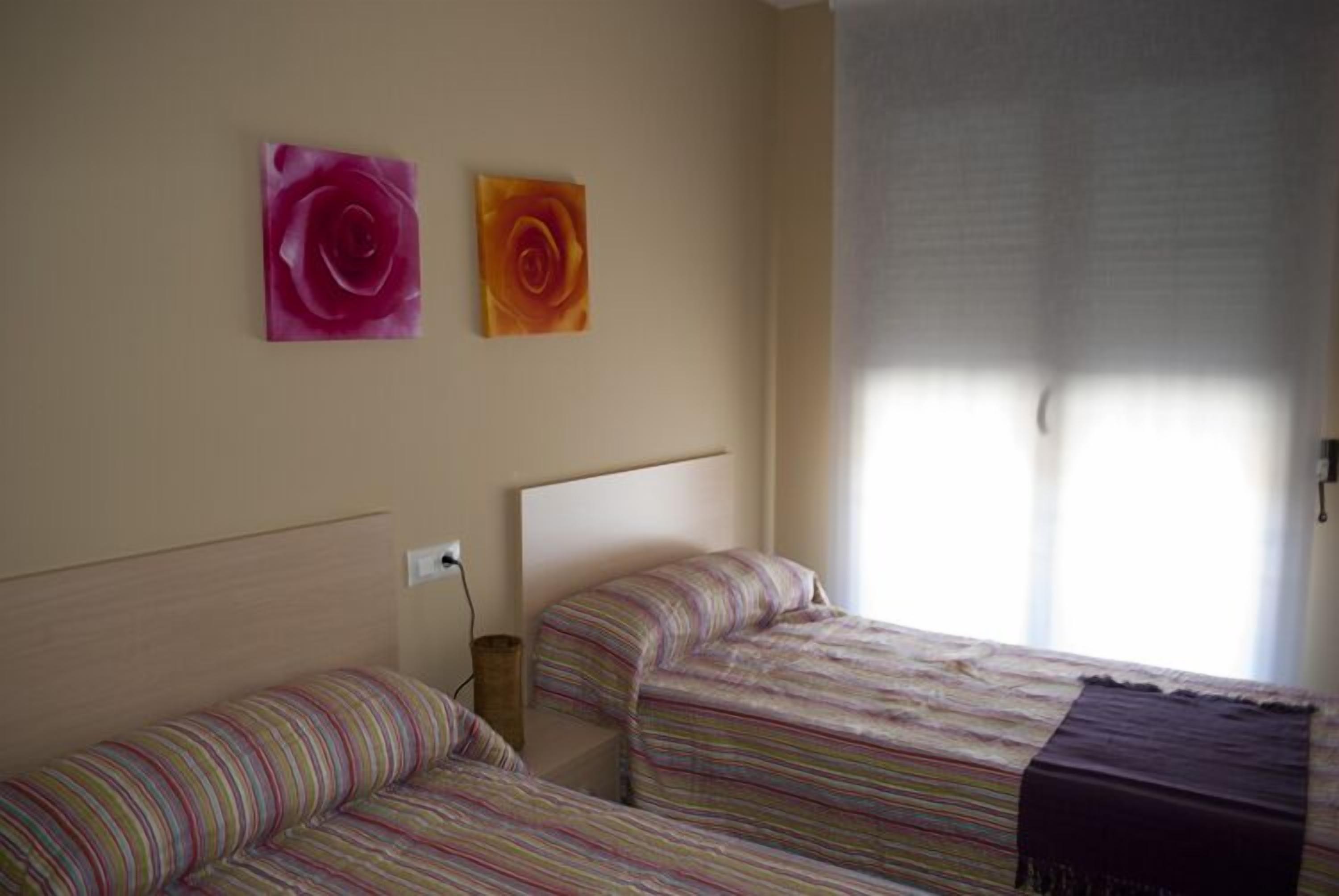 Un dormitorio con dos camas, cada una con ropa de cama a rayas, cabeceros lisos y dos cuadros de rosas colgados en la pared.