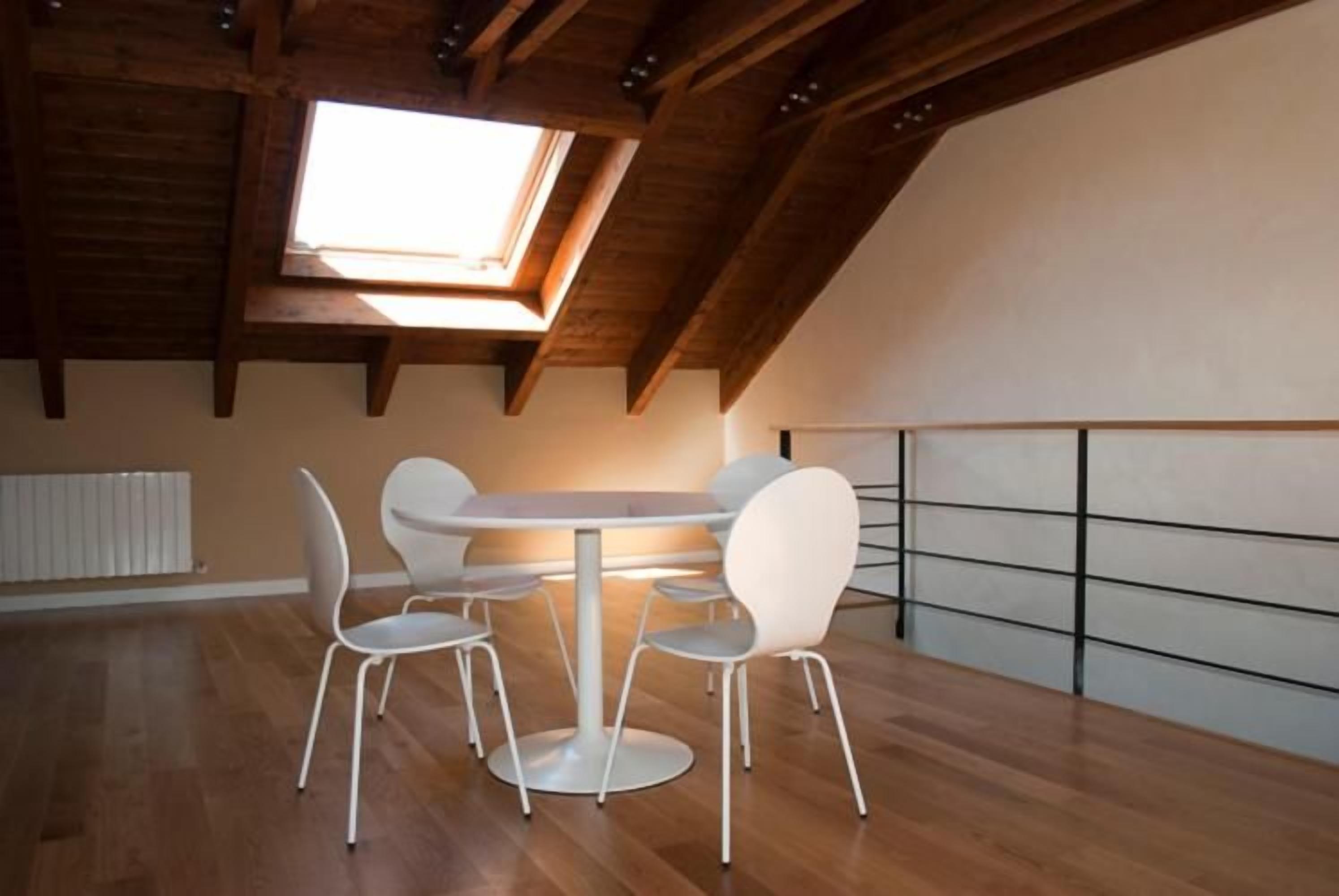 Una habitación con tragaluz, vigas de madera, una mesa redonda con sillas y un radiador blanco.