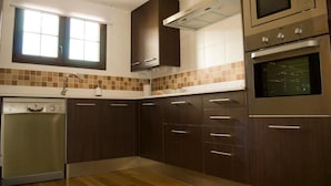 A modern kitchen with dark wooden cabinets, a built-in dishwasher, a double oven, and a window above the sink. - Residencial Massana (Alcala de la Selva)