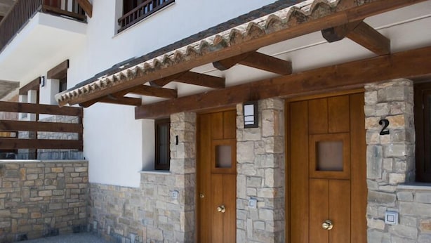 A building with two wooden doors, stone walls, and a wooden balcony. - Residencial Massana (Alcala de la Selva)