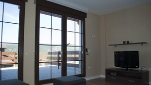 A living room with a large sliding glass door leading to a patio, a flat-screen TV on a wooden stand, and a small shelf above the TV. - Residencial Massana (Alcala de la Selva)