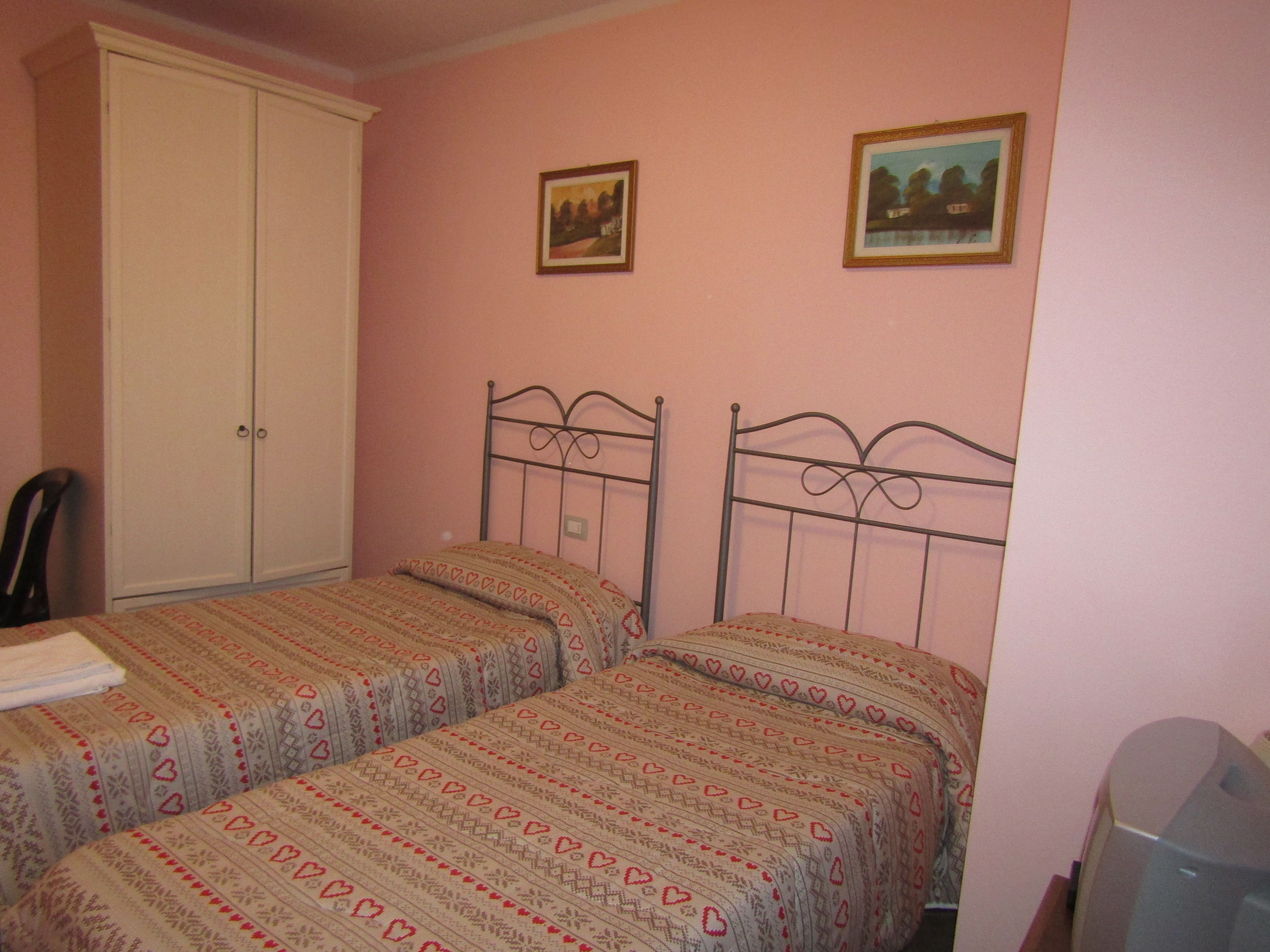 A bedroom with two beds, a wardrobe, and two framed pictures on the wall.
