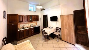 Une cuisine compacte avec des meubles en bois, une table à manger avec des chaises, un téléviseur fixé au mur et une armoire.