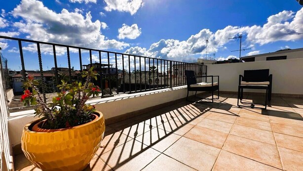 Une terrasse sur le toit, agrémentée d’un jardinier jaune, d’une rambarde en métal et surplombant un ciel d’un bleu limpide.