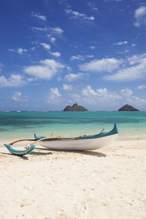 Un bateau sur une plage de sable fin, avec une eau turquoise et limpide, et deux petites îles qui se dessinent à l’horizon.
