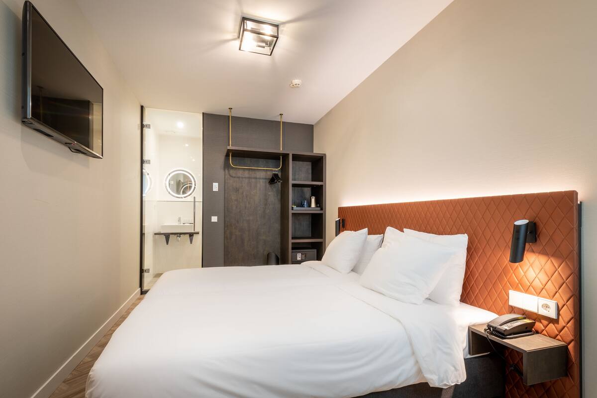 A modern hotel room with a large bed, a TV mounted on the wall, a vanity with a mirror, and a built-in wardrobe.