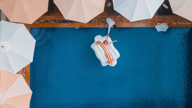 A person floating on an inflatable ring in a swimming pool with multiple umbrellas around. - Popular Hotel & Spa (Siem Reap)