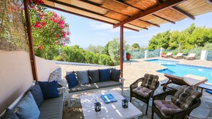 An outdoor seating area with a pool, stone flooring, and a pergola. - Angelina Studios (Skiathos)