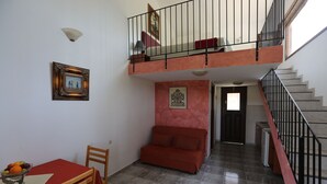 A dining area with a table and chairs, a sofa, a staircase, and a hallway leading to another room. - Angelina Studios (Skiathos)