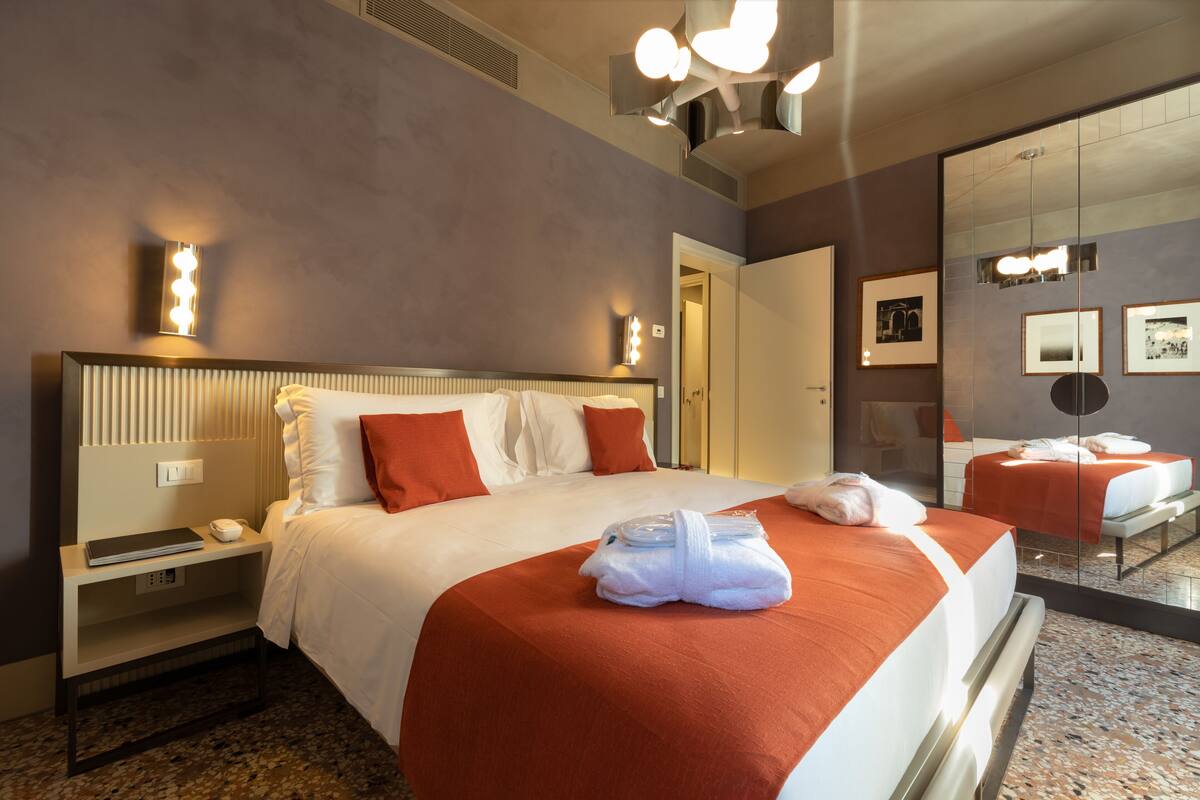 A hotel room with a large bed, a bedside table, a mirror, and a wall-mounted light fixture.
