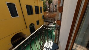 En smal balkon med gelænder, en grøn stol og udsigt til en gul bygning med mange vinduer.