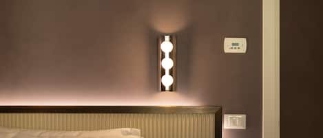 A hotel room with a bed, a wall-mounted light fixture, and a thermostat.
