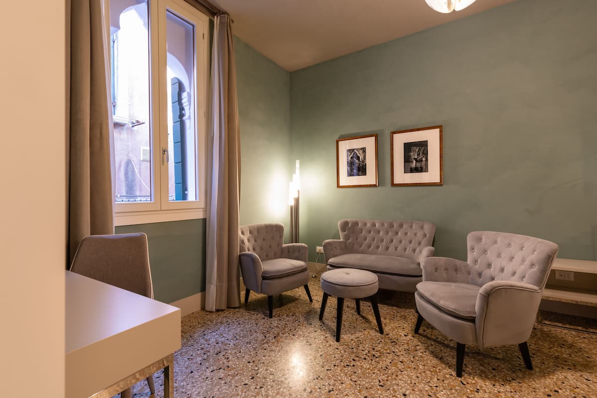 A room with a dining table, two armchairs, a sofa, a floor lamp, and two framed pictures on the wall.