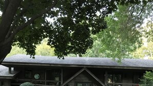 A rustic lodge with a large stone centerpiece in the garden, surrounded by well-maintained greenery and a wooden deck.
