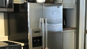 A kitchen with a microwave, oven, refrigerator, and a three-tiered fruit and vegetable stand.