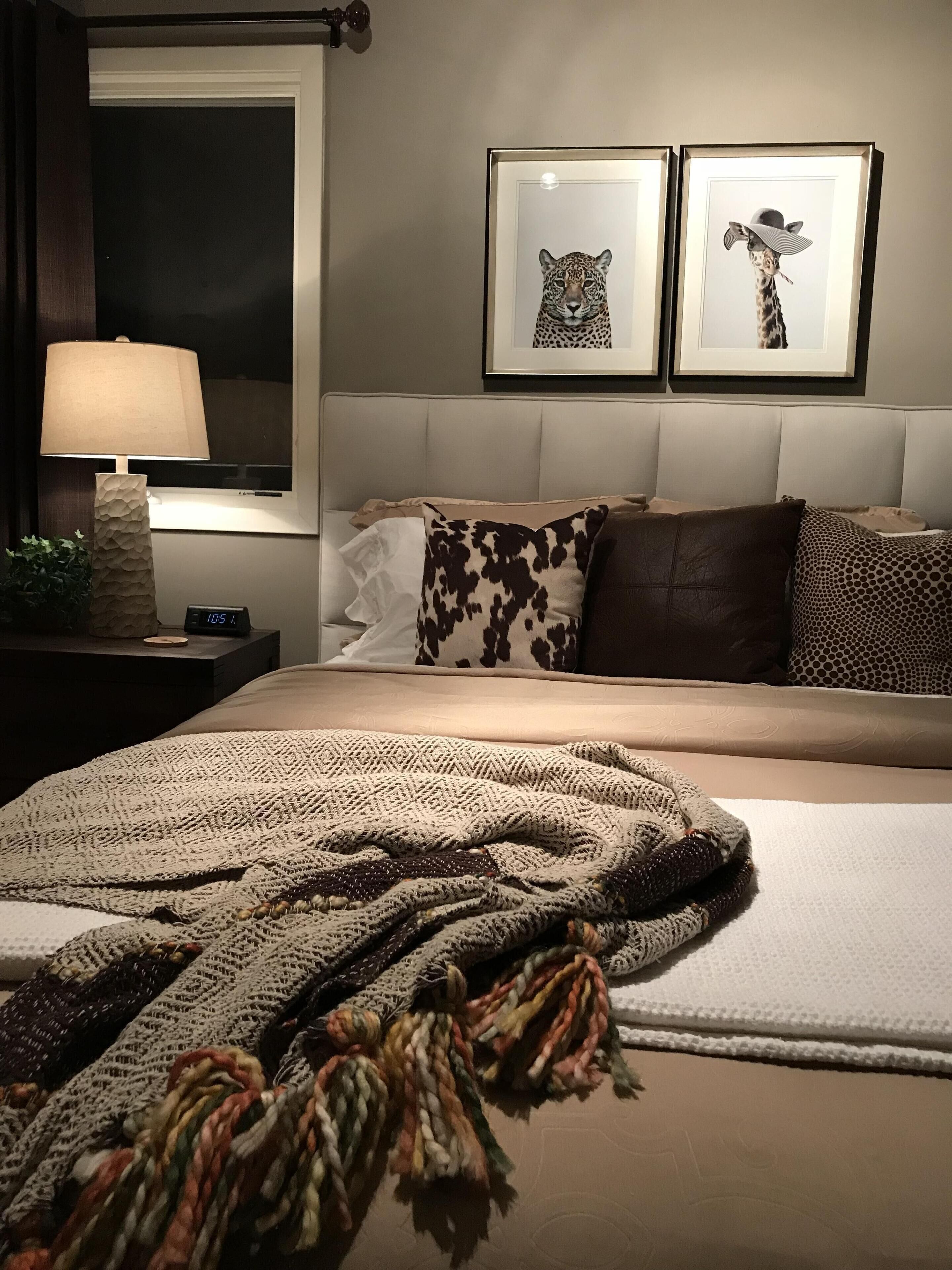 Une chambre à coucher avec un lit, une table de chevet avec une lampe, une horloge numérique et deux tableaux encadrés accrochés au mur.