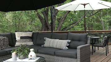 A deck with a gray sofa, a round coffee table, and two umbrellas.