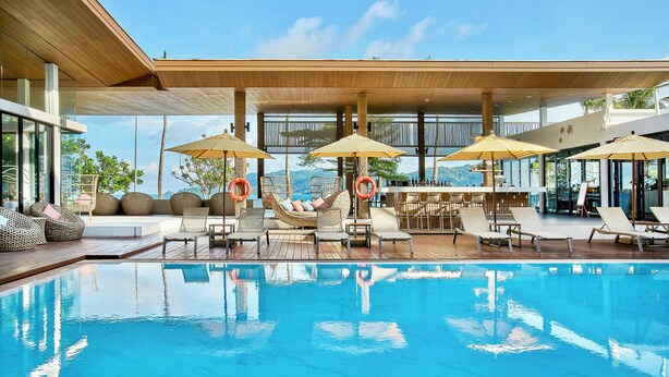 A modern pool area with lounge chairs, umbrellas, and a clear view of the mountains. - LIV Hotel Phuket Patong Beachfront (Patong)
