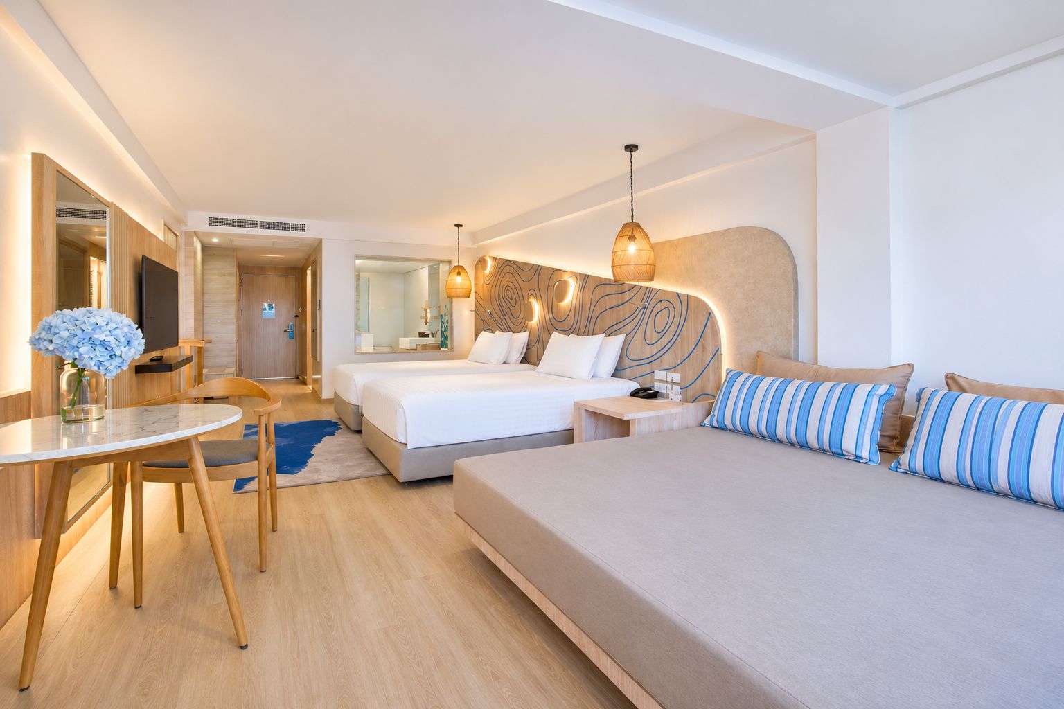 A hotel room with a large bed, a smaller bed, a desk with a chair, a round table, and a mirror.