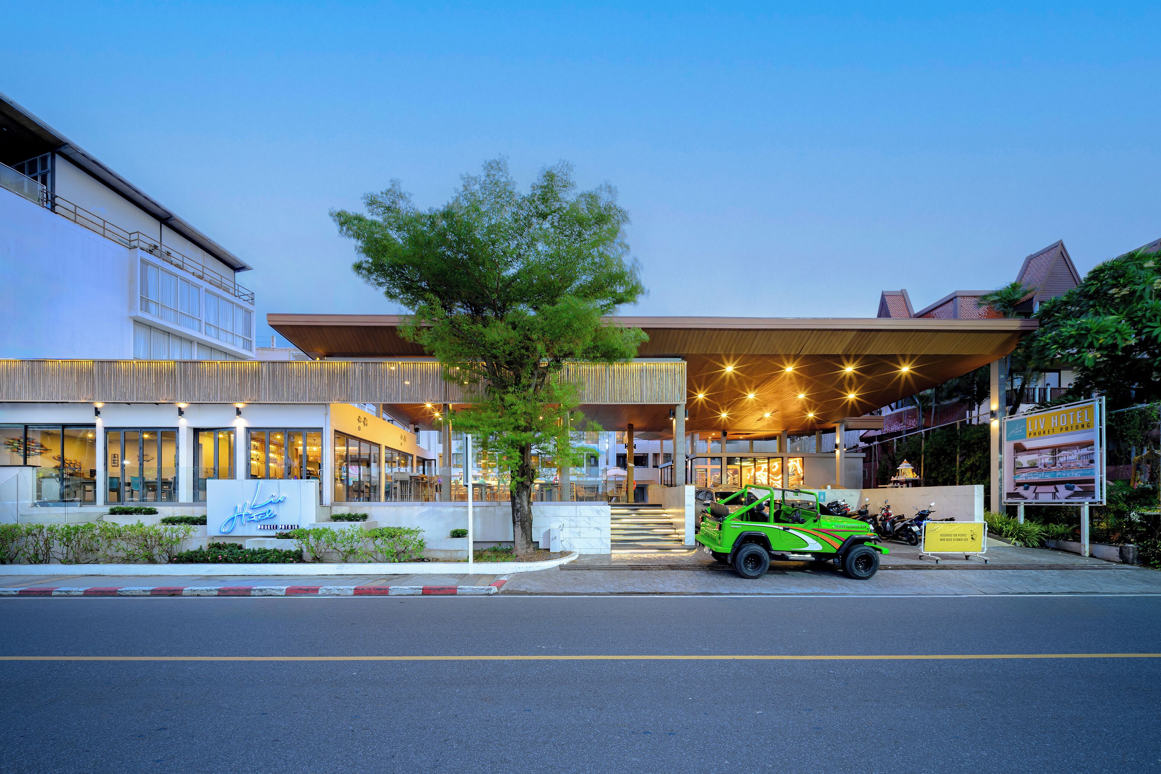 A hotel with a modern design, a green car parked in front, and a sign for the hotel.