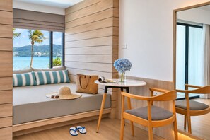 Una habitación con vistas al mar, una pared de madera, un rincón con cojines junto a la ventana, una mesa con un jarrón y dos sillas.