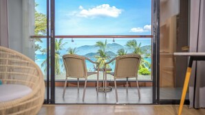 A balcony with wicker chairs, a small table, and a view of the ocean and palm trees. - LIV Hotel Phuket Patong Beachfront (Patong)