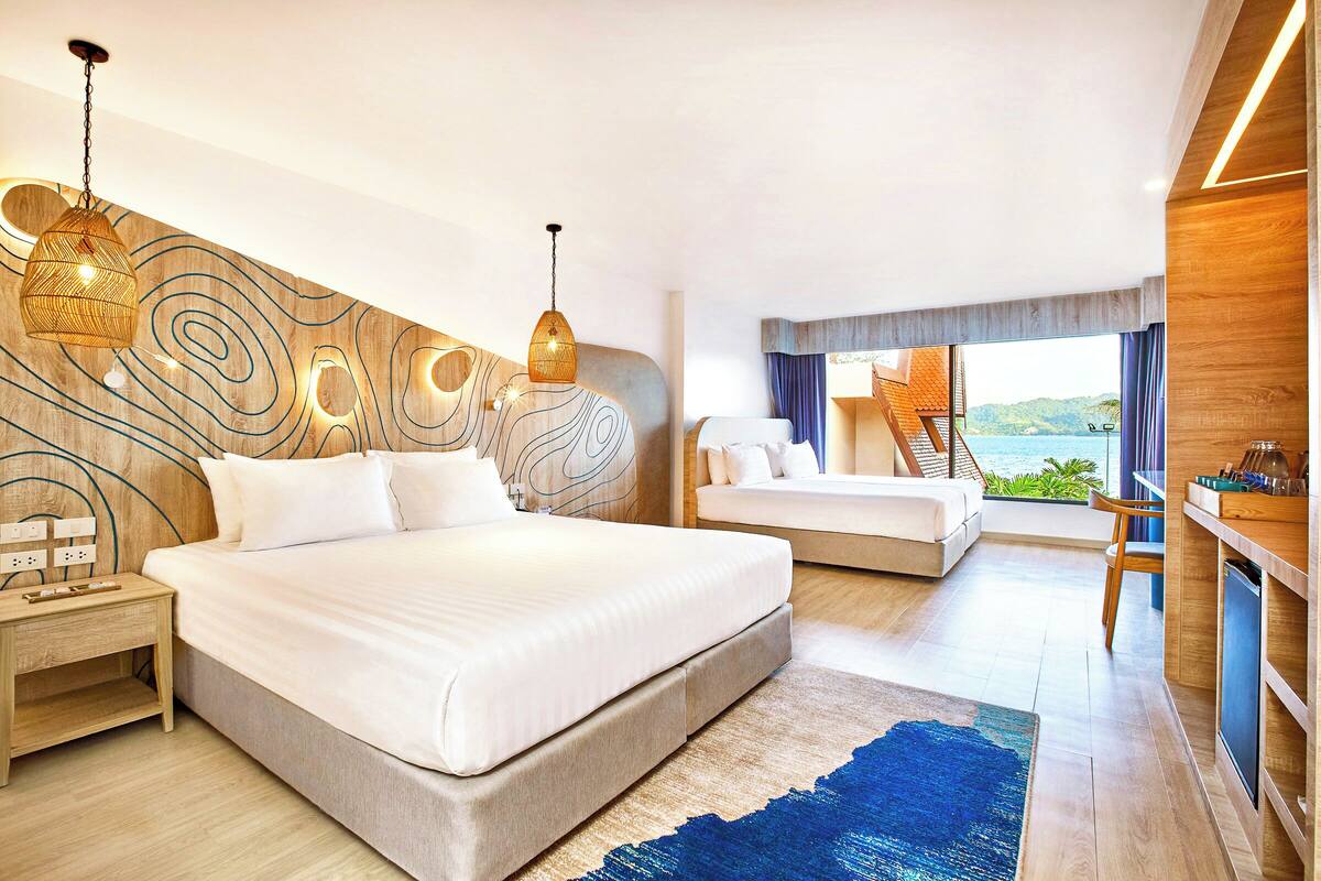 Een moderne hotelkamer met een groot bed, twee nachtkastjes, een bureau en uitzicht op zee.