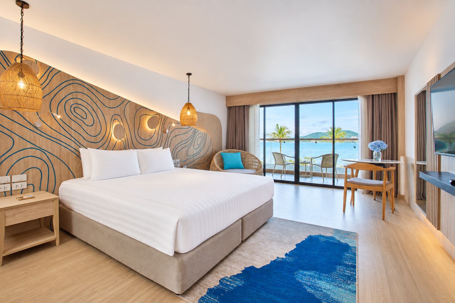 A modern hotel room with a large bed, a dining area, and a view of the sea.
