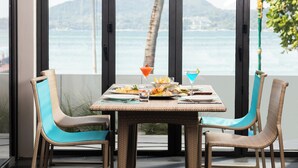 A dining table with chairs, a view of the sea, and mountains in the background. - LIV Hotel Phuket Patong Beachfront (Patong)