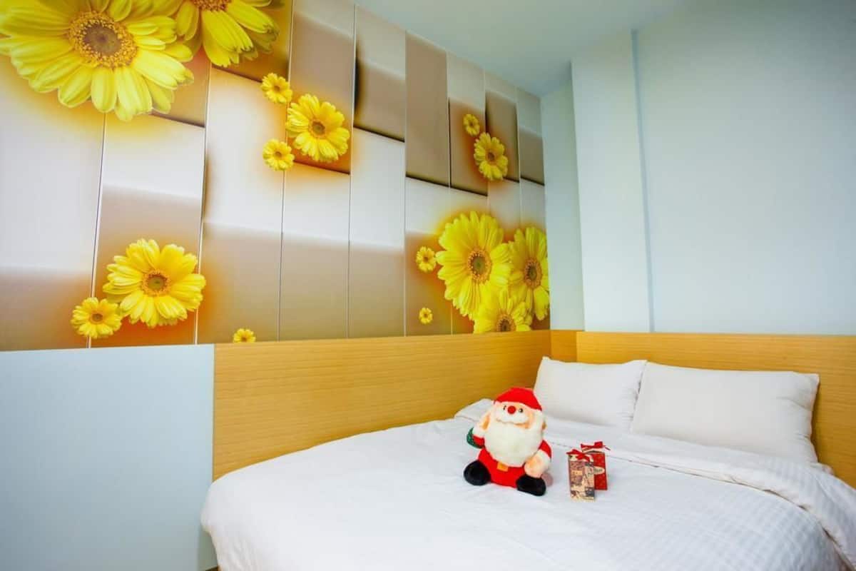 A hotel room with a bed, a plush Santa toy, and a wall decorated with large yellow flowers.