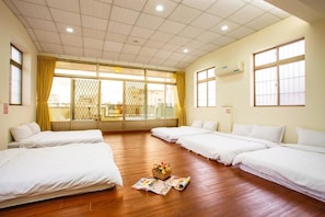 A hotel room with four single beds, wooden flooring, a large window with curtains, and a small table with a basket of fruit. - Haian Star (Tainan)