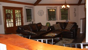 A living room with a brown leather sofa, a wooden coffee table, and a chandelier. There are windows with curtains and a door with glass panels. - Canyon Lake Texas Hill Country (Canyon Lake)