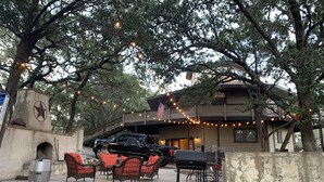 An outdoor seating area with wicker chairs and a grill, under a large tree with string lights. - Canyon Lake Texas Hill Country (Canyon Lake)