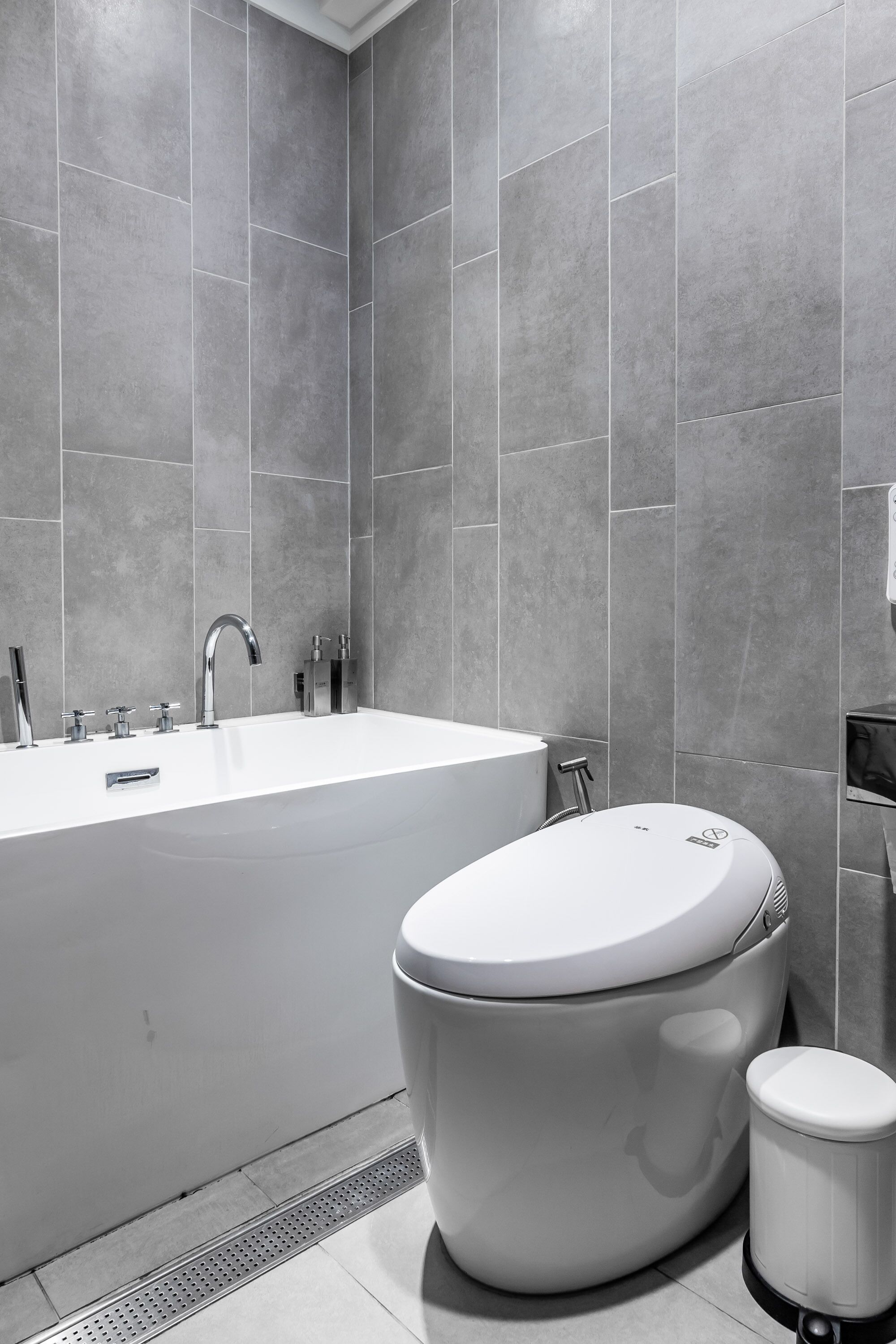 A modern bathroom with a large white bathtub, a toilet, and a trash can.