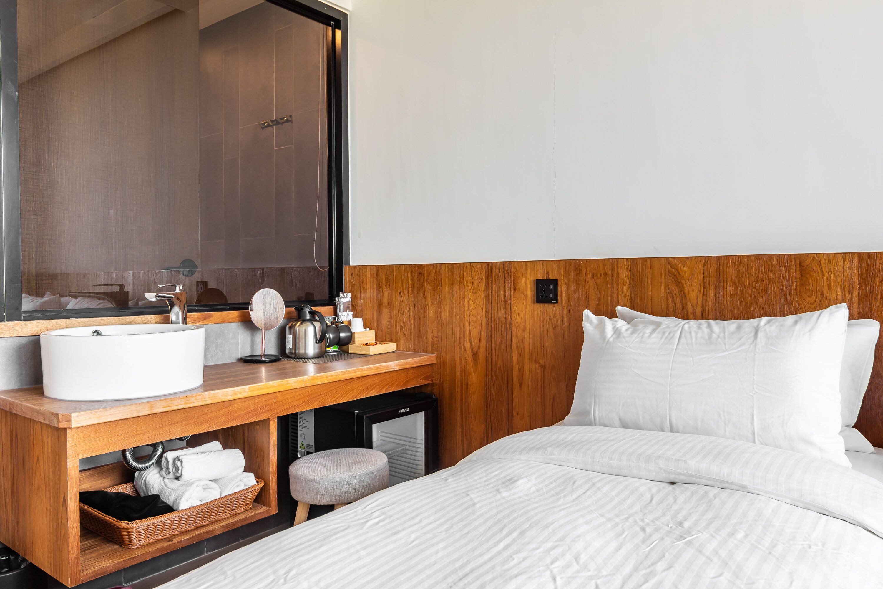 A hotel room with a wooden headboard, a large mirror, a wooden vanity with a sink, a small heater, and neatly made bed with white bedding.