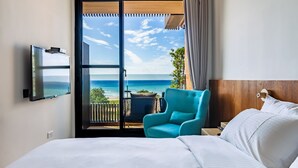 A hotel room with a bed, a TV, a blue chair, and a balcony with a view of the ocean. - Kenting seawall Inn 112 (Hengchun)