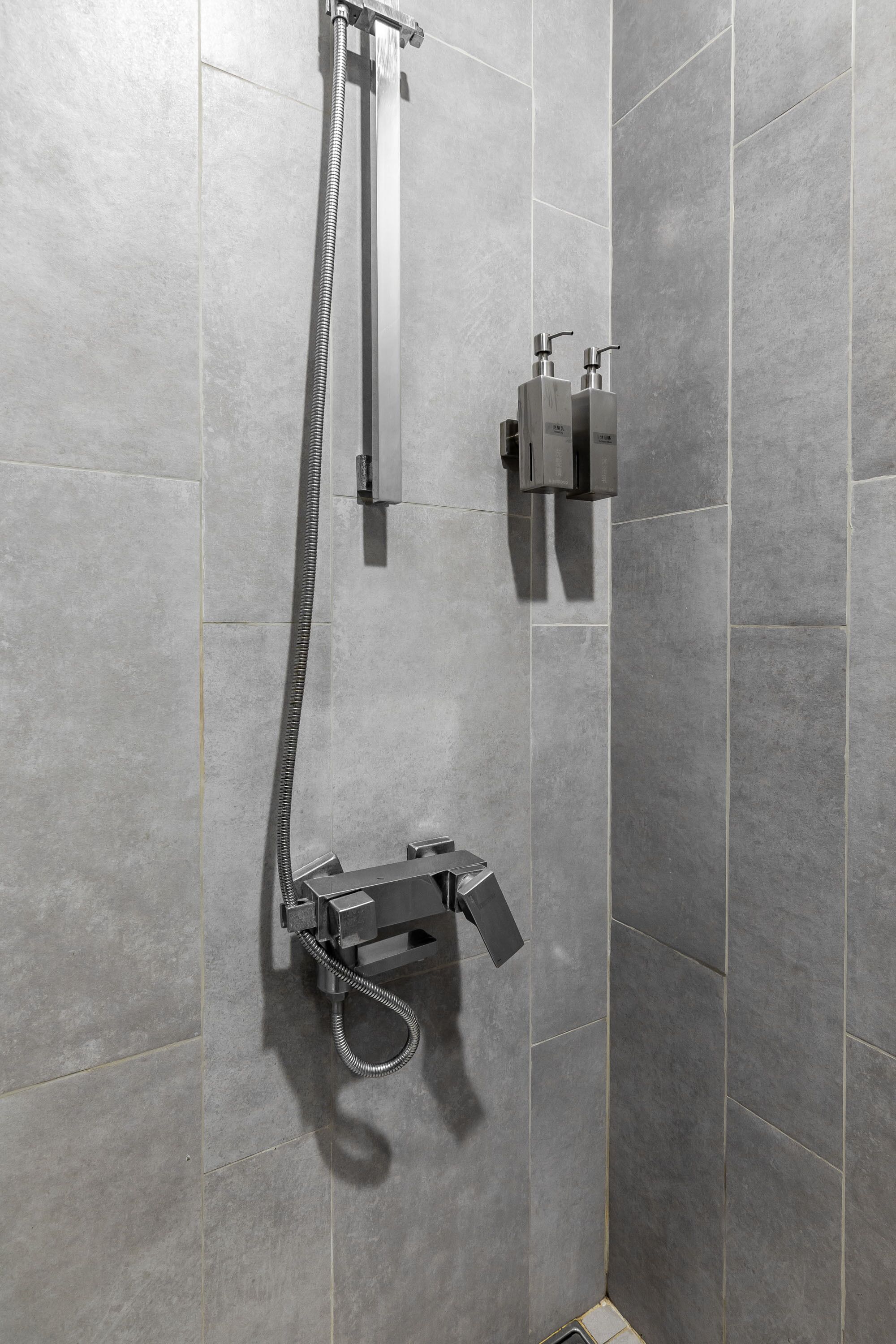 Une douche équipée d’un pommeau de douche à main et d’un robinet fixé au mur.