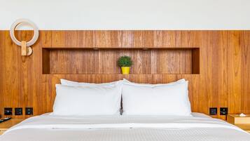 A neatly made bed with white linens, a wooden headboard, and a small potted plant on the shelf above.