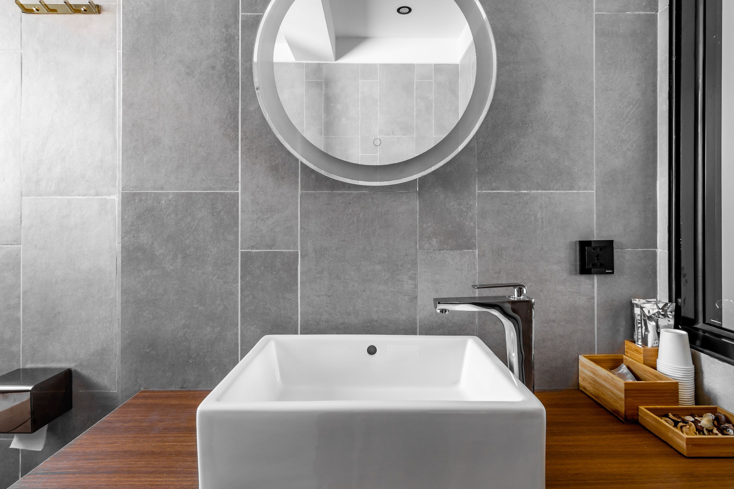 A modern bathroom with a rectangular sink, a round mirror, and a wooden vanity.
